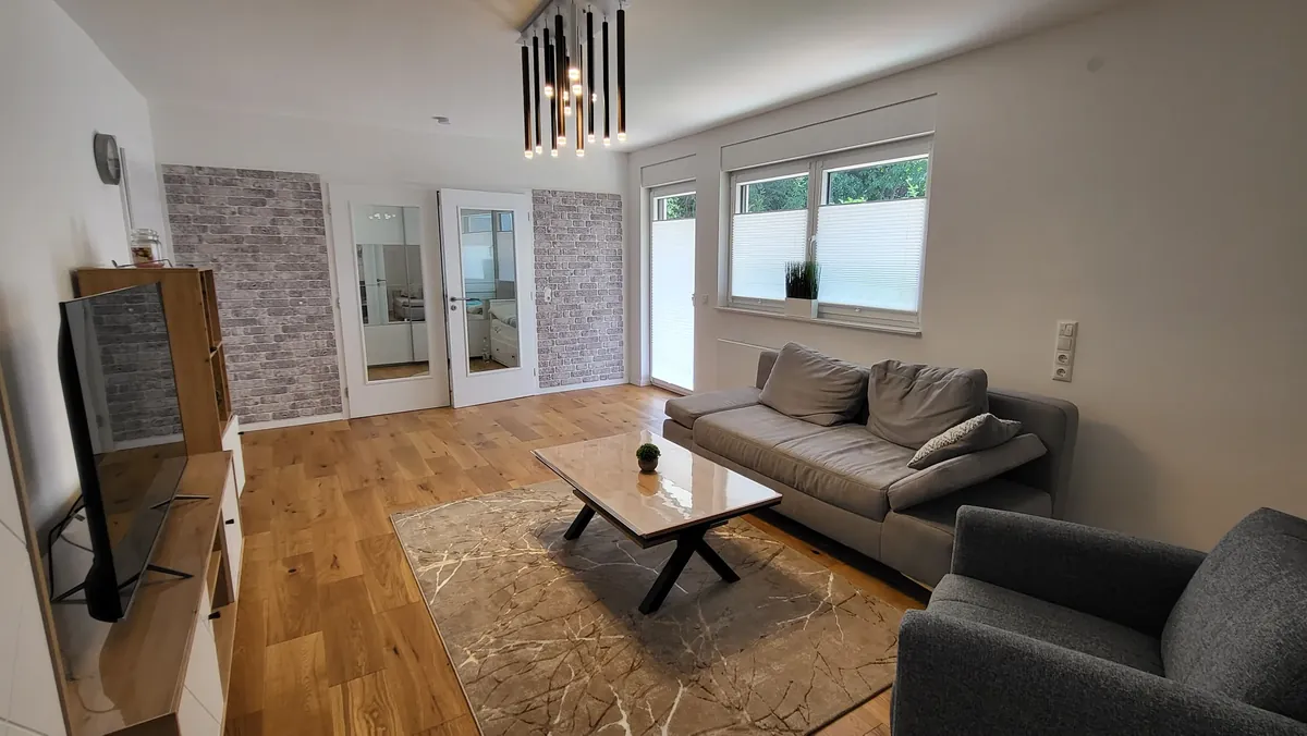Wohnbereich mit Sofa, Ziegelwand und Terrassentür – Deluxe Apartment mit Garten, Quiet Apartments Bergisch Gladbach-Refrath